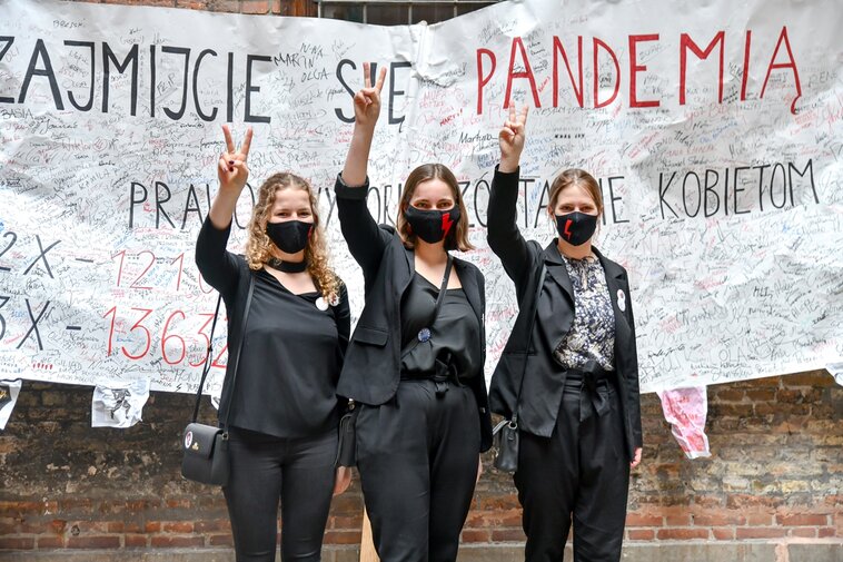 Zdjęcie. Julia Landowska, Marianna Łoboda i Aleksandra Łoboda z uniesionymi dłońmi z symbolem zwycięstwa. W tle fragment transparentu z niewidocznymi podpisami.  