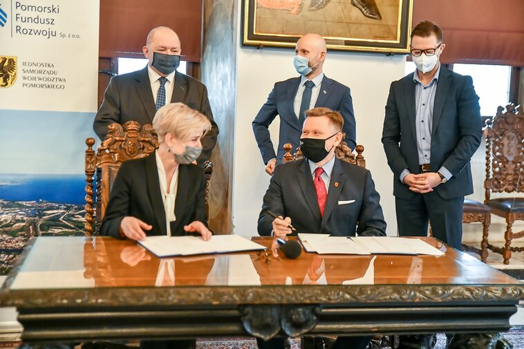 Zdjęcie. Od lewej siedzą: Irena Wróblak, Prezes Zarządu Pomorskiego Funduszu Rozwoju oraz Waldemar Ossowski, dyrektor Muzeum Gdańska. Podpisują umowę. Za nimi stoją Wiesław Byczkowski, Wicemarszałek Województwa Pomorskiego, Alan Aleksandrowicz, z-ca Prezydenta Gdańska oraz Adam Zalewski z PFR. 