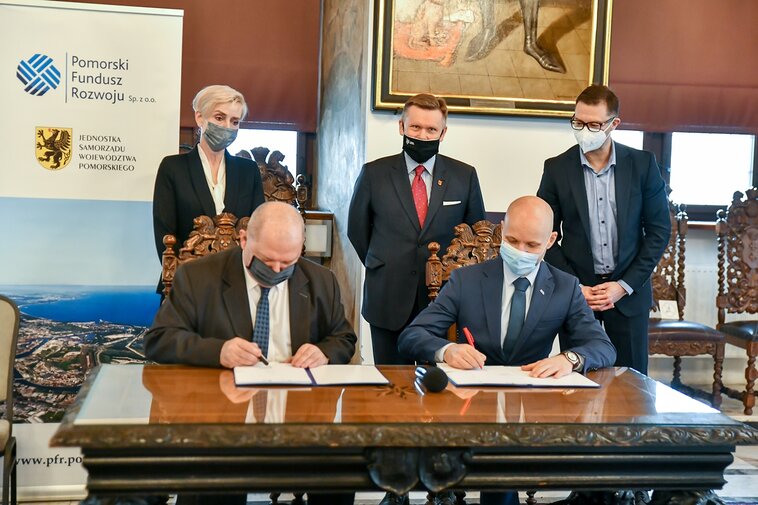 Zdjęcie. Od lewej siedzą: Wiesław Byczkowski, Wicemarszałek Województwa Pomorskiego i Alan Aleksandrowicz, z-ca Prezydenta Gdańska. Podpisują umowę. Za nimi stoją  Irena Wróblak, Prezes Zarządu Pomorskiego Funduszu Rozwoju, Waldemar Ossowski, dyrektor Muzeum Gdańska oraz Adam Zalewski z PFR. 