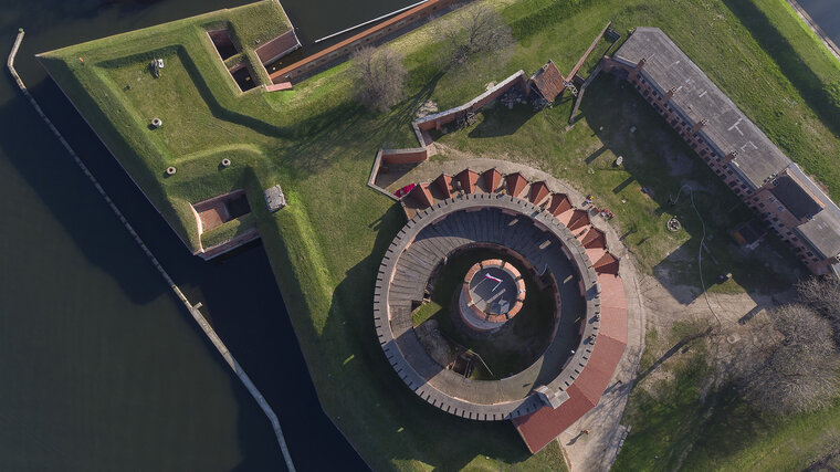 Zdjęcie. Twierdza Wisłoujście. Fort Carre i cylindryczna wieża z lotu ptaka. Nad wieżą widoczny fragment północnego muru oporowego i drewniana wiata.    