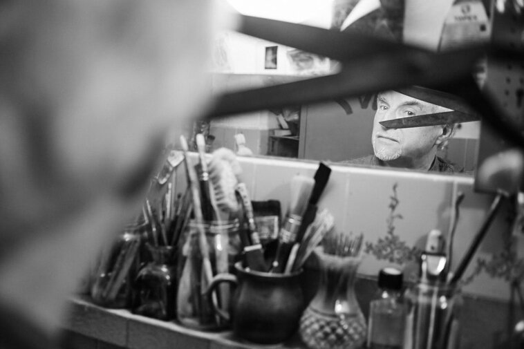 Zdjęcie czarno-białe. Mężczyzna z nożyczkami przegląda się w lustrze.