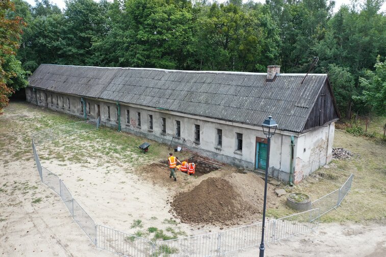 Zdjęcie „z lotu ptaka”. W centrum podłużny budynek koszar napoleońskich. Widoczne okna oraz wykop archeologiczny i archeolodzy.   