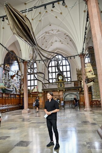 Zdjęcie. Oskar Zięta w Wielkiej Hali Dworu Artusa. Nad nim rzeźba krakena. 