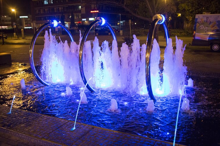 Zdjęcie. Wieczór. Fontanna Heweliusza - iluminowany pokaz wodny. W tle ulica.  