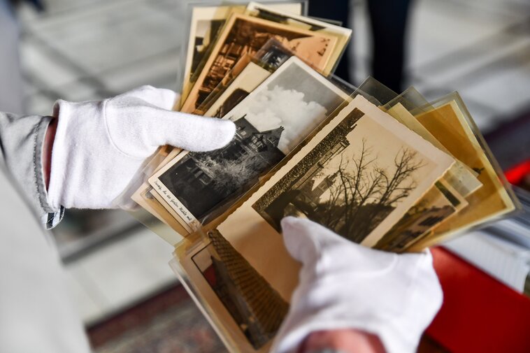 Zdjęcie. W dłoniach pocztówki z widokami Gdańska. W tyle kaseta z resztą pamiątek.  