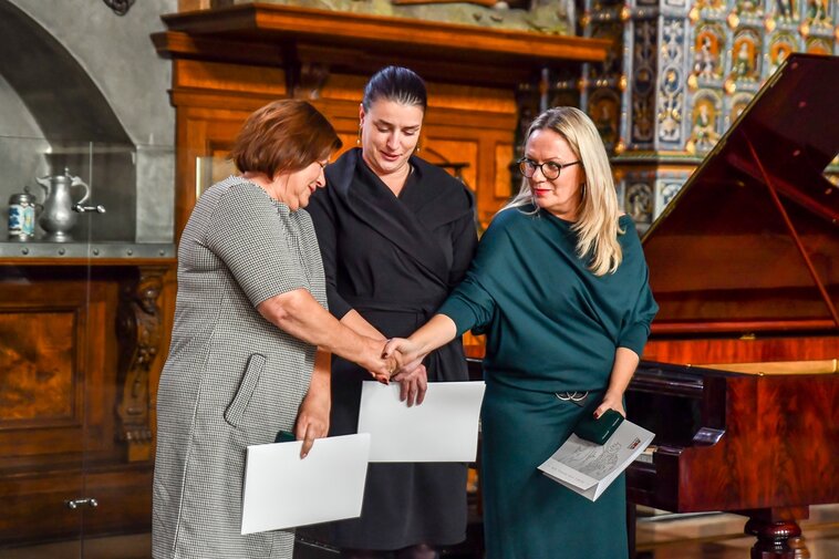 Od lewej Ewa Joszczak, Kinga Krause oraz Ewa Joszczak z dyplomami Medali Prezydenta Miasta Gdańska. Trzymają się za dłonie. 