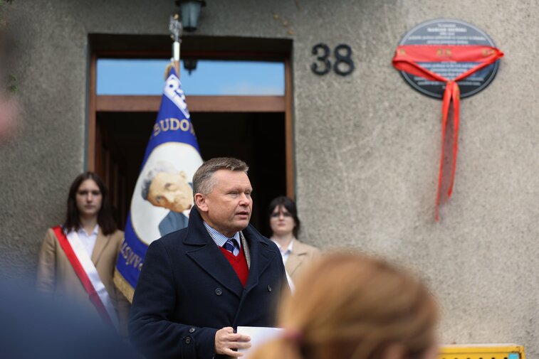 Zdjęcie z uroczystości odsłonięcia pamiątkowej tablicy. Przemawia Waldemar Ossowski, dyrektor Muzeum Gdańska, w tle widać tablicę na elewacji przepasaną wstęgą z logotypem miasta. 