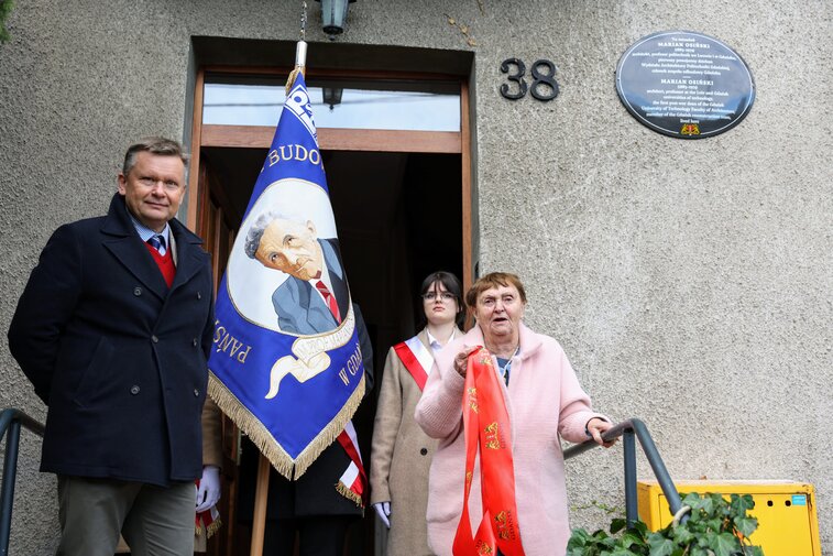 Zdjęcie przy wejściu do domu, na którego elewacji zawisła pamiątkowa tablica. Po lewej stronie stoi Waldemar Ossowski, dyrektor Muzeum Gdańska, z prawej strony stoi Maria Osińska, synowa profesora. Widać także poczet sztandarowy i sztandar szkoły, na którym znajduje się wizerunek profesora Osińskiego. 