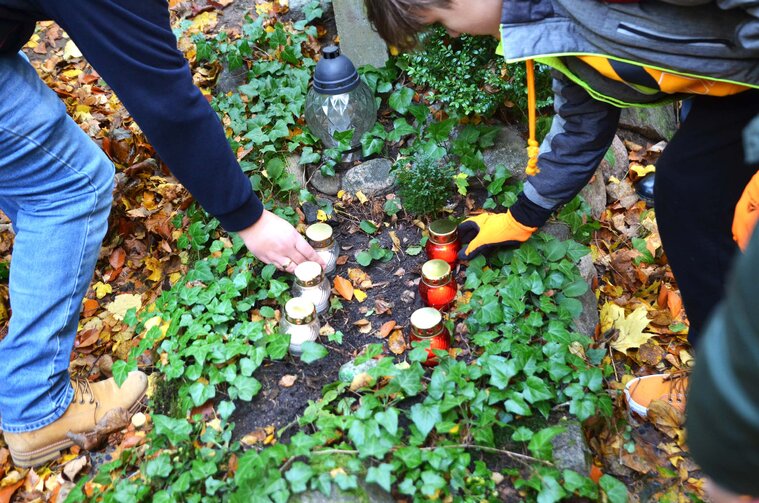 Zdjęcie. Uczniowie porządkujący nagrobek zarośnięty trawą. 