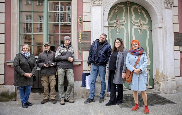 Zdjęcie. Przed fasadą Domu Uphagena. Od lewej Ewa Szymańska, Remigiusz Pacer z łupą żelaza, Grzegorz Ciechomski, Bartosz Nawacki, Anna Kriegseisen oraz Katarzyna Darecka.   