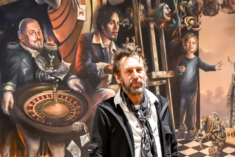 Zdjęcie. Tomasz Sętowski. W tle obraz "Czyściec" z trzema postaciami. W środku postać artysty.