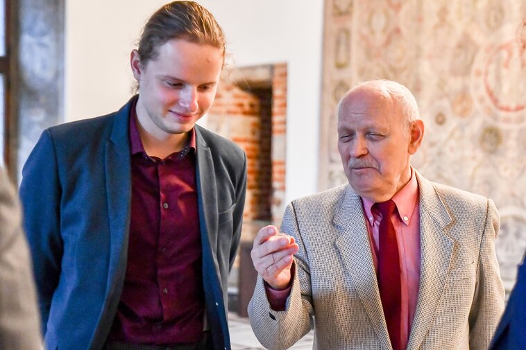 Zdjęcie. Filip Ogłuszka i uśmiechnięty Bogusław Kaczmarek. Ostatni trzyma w dłoni przekazanego do Muzeum szeląga. 