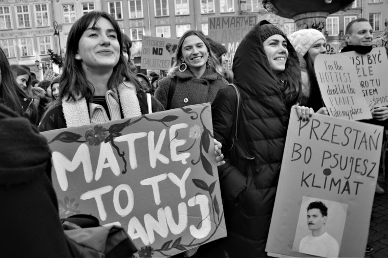 Czarno-białe zdjęcie. Kobiety na Długim Targu w Gdańsku. Trzymają transparenty z napisami. Na pierwszym planie kobieta z napisem: "Matkę to ty szanuj". 