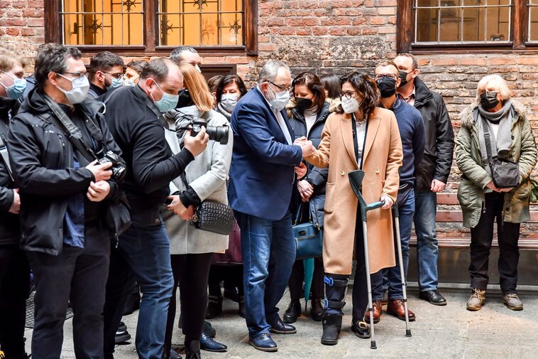 Zdjęcie. Aleksandra Dulkiewicz trzyma się za rękę z Piotrem Adamowiczem. W tle uczestniczy wernisażu. 