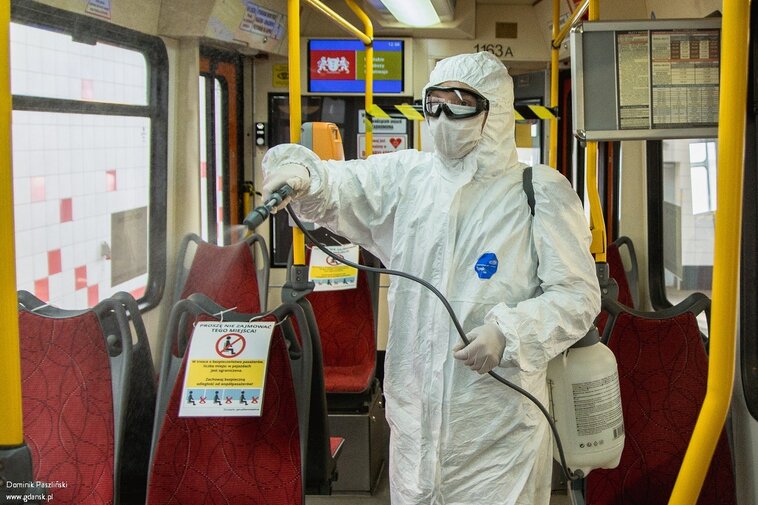 Zdjęcie. Wnętrz tramwaju. Pracownik w kombinezonie ochronny dezynfekuje siedzenia. 