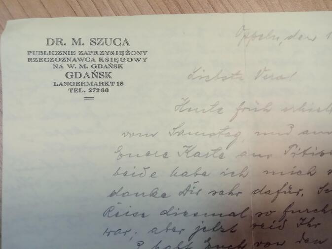 Zdjęcie. Fragment listu na papierze firmowym. W lewym górnym rogu dane adresowe Michała Szucy w języku polskim. Pismo odręczne niżej. Treść w języku niemieckim. 