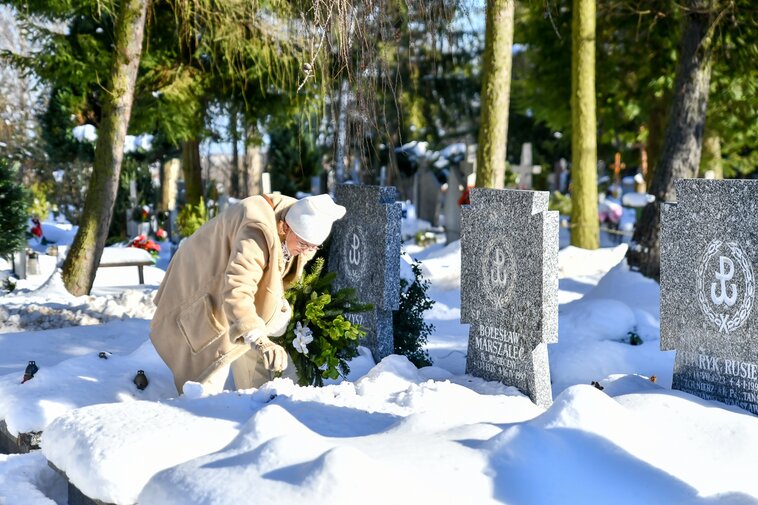 Na zdjęciu seniorka porządkująca jeden z nagrobków. 