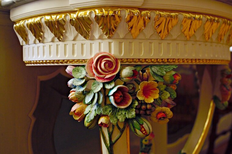 Zdjęcie. Fragment stolika konsolowego. Widoczne ornamenty kwiatowe i złocone liście. 