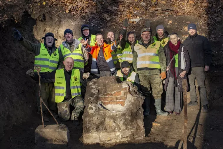 Zdjęcie. Grupa archeologów stojąca w otoczeniu pozostałości grobu Nataniela Wolfa. 