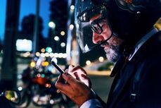 Small_MS PPT_MS Word_Newsletter-A man wearing a motorcycle helmet looks at his phone outside at night.jpg
