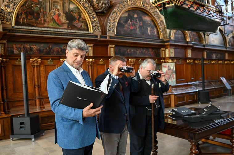 Zdjęcie. Zbliżenie, kobieta robi zdjęcie telefonem otwartemu albumowi. W środku zabytkowe zdjęcia Gdańska.