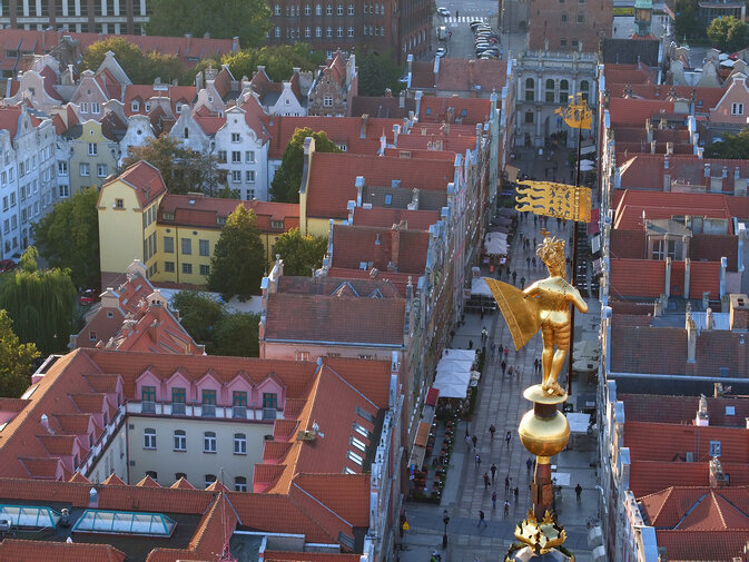 Zdjęcie przedstawia widok z loty ptaka na ulicę Długą w kierunku Złotej Bramy. Na kamienice spogląda pozłacana figura król Zygmunta Augusta odwrócona tyłem do widza. Król trzyma proporzec. 