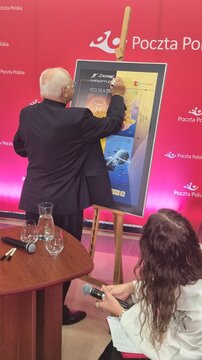 Wojciech Siudmak podpisał plakat prezentujący znaczki z jego dziełami 