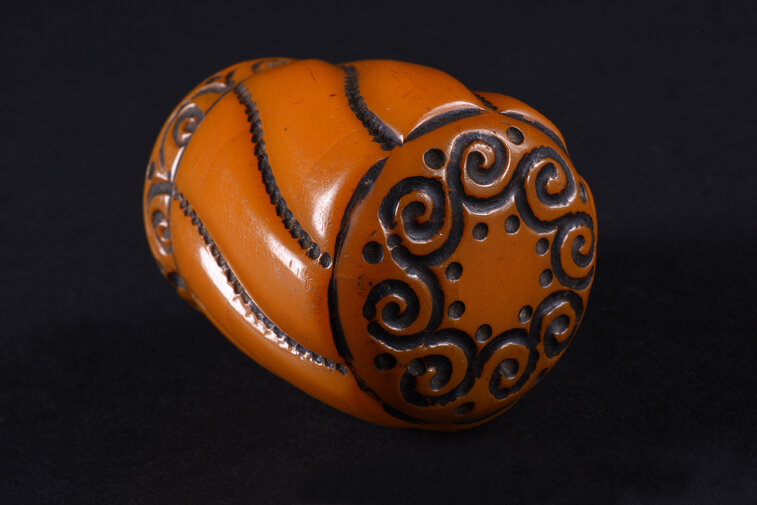 Gałka do laski w formie obłego, lekko zwężającego się ku dołowi walca, o dwóch podstawach w formie koła. Gałka rozczłonkowana po obwodzie przez esowate linie utworzone przez gęsto ułożone kropki. Górna podstawa dekorowana w koło ornamentem pojedynczych, połączonych ze sobą spirali, przy łączeniu ujętych po bokach dwoma kropkami. Dolna partia gałki dekorowana wąskim fryzem z ornamentem tworzonym przez szereg pojedynczych spirali w półłuku, między półłukami pojedyncza kropka.