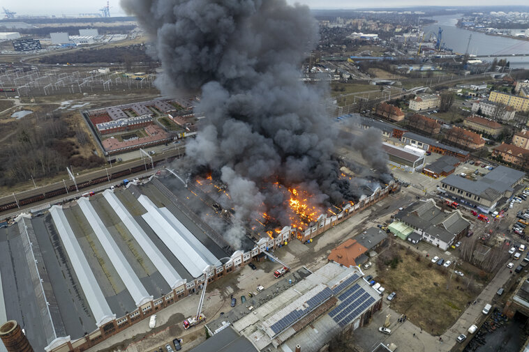 Widok z lotu ptaka na ogromny pożar hali przemysłowej. Z budynku wydobywają się płomienie i gęsty czarny dym, wokół zabudowa dzielnicy Przeróbka.