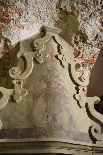 Zdjęcie przedstawia dekorację osiemnastowiecznego kominka w Domu Komendanta Twierdzy Wisłoujście. Ozdobiony jest kolorową polichromią przedstawiającą wazon z kwiatami.