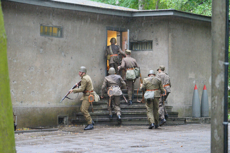 Zdjęcie przedstawia rekonstrukcję walk w obronie Westerplatte 1-7 września 1939 r. Widocznych kilku rekonstruktorów w polskich mundurach wbiegających do budynku wartowni. 