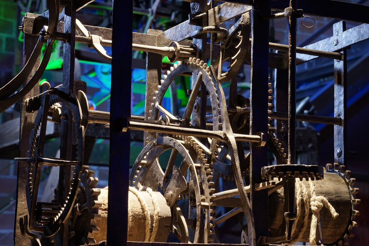 Zdjęcie przedstawia mechanizm starego zegara wieżowego. Zbliżenie na koła zębate i przekładki. 