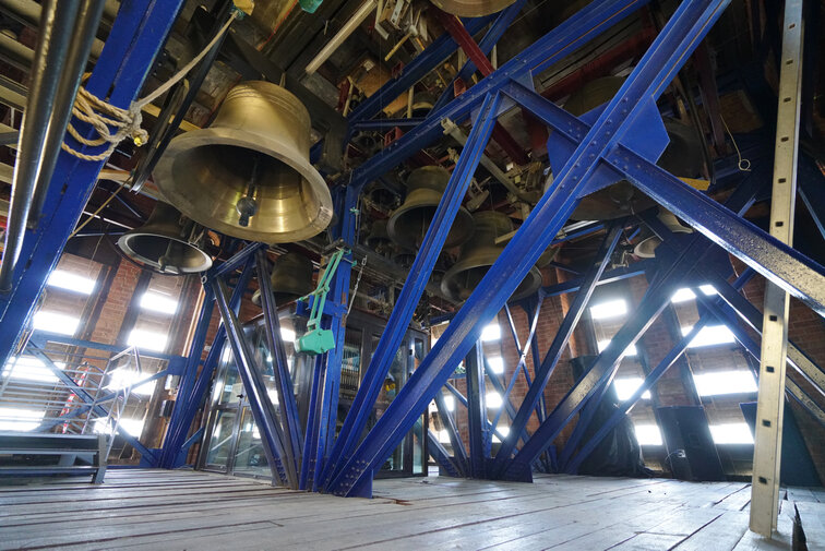 Zdjęcie wykonane w wieży kościoła św. Katarzyny (Muzeum Nauki Gdańskiej). Widok na zespół dzwonów – carillon, zawieszony na stalowej konstrukcji. Na pierwszym planie widoczny od dołu jeden z dzwonów. 