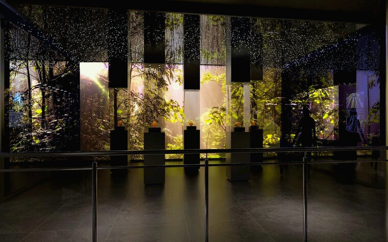 Wizualizacja przedstawia wnętrza Wielkiego Młyna. Widok z frontu na instalację "las bursztynowy". W głębi imitacja lasu, z przodu ciemne pylony, które w połowie wysokości są przeszklone. W środku każdego z pięciu pylonów znajduje się bryła bursztynu.   