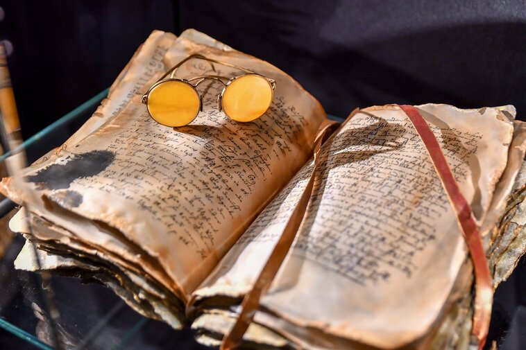 Zdjęcie. Okulary z bursztynowymi soczewkami położone na książce.   