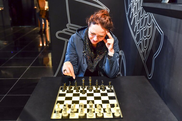 Zdjęcie. Kobieta siedząca przy stole z szachownicą. 