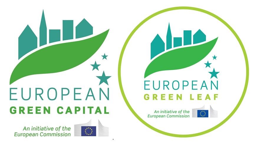 W graficy przeważają barwy zielone. Widać kształt liści nad którym umieszczono zarysy zabudowań. Widać też zielone gwiazdki. Z prawej strony jasnozielony okręg. Pod grafikami napisy European Green Capital 2022 oraz European Green Leaf