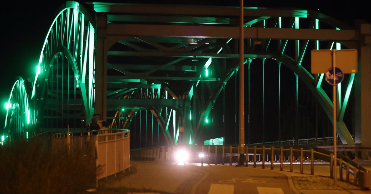 Na zdjęciu widoczna jest konstrukcja wiaduktu w kształcie łuków. Wiadukt jest podświetlony w kolorze zielonym.