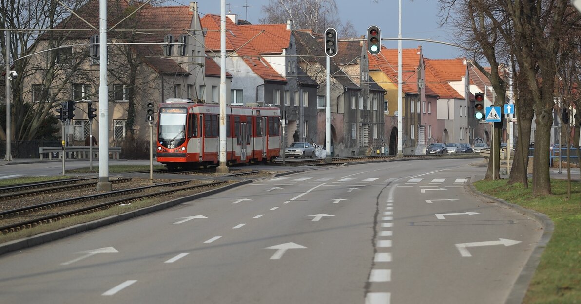 Na fotografii widoczna jest dwupasmowa, szara jezdnia ulicy Hallera. Obok jezdni widoczne są tory tramwajowe, po których jedzie czerwono-kremowy tramwaj. W tle szereg domków jednopiętrowych.