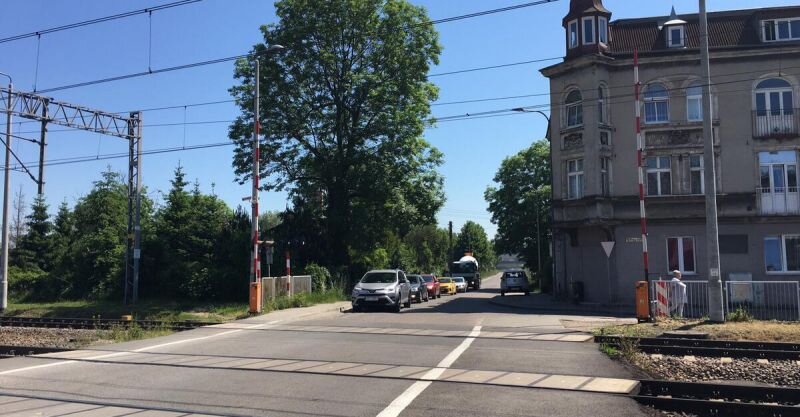 Na zdjęciu widoczny jest przejazd kolejowy w ciągu ul. Sandomierskiej. Szlabany są otwarte, na przejazd wjeżdżają samochody.