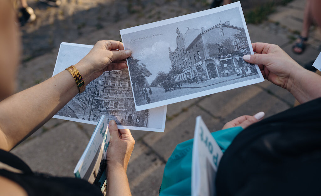 Zdjęcie przedstawia fotografie/ryciny starego Gdańska, trzymane przez dwie osoby. Widok z góry nie widać osób, tylko reprodukcje w dłoniach.