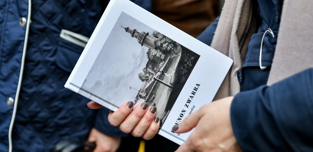 Dłonie trzymają książkę "W gdańskiej Twierdzy" autorstwa Brunona Zwarry. Książka ma białą okładkę. Na ilustracji sylwetka wieży Twierdzy Wisłoujście. 