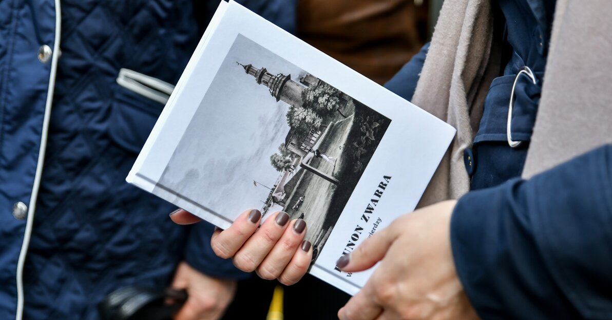 Dłonie trzymają książkę "W gdańskiej Twierdzy" autorstwa Brunona Zwarry. Książka ma białą okładkę. Na ilustracji sylwetka wieży Twierdzy Wisłoujście. 