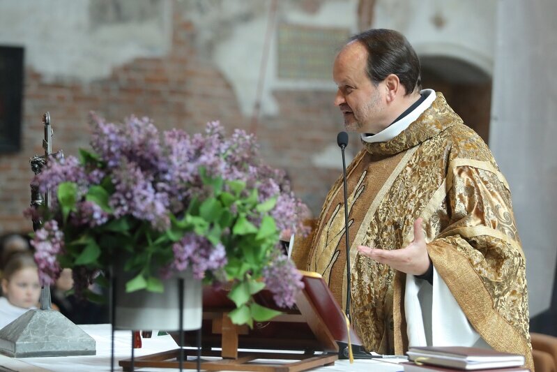 Na zdjęciu widoczny jest ksiądz Niedałtowski w złotej szacie liturgicznej. Ksiądz stoi przodem do ołtarza na którym stoi krzyż i wazon z fioletowymi kwiatami bzu.