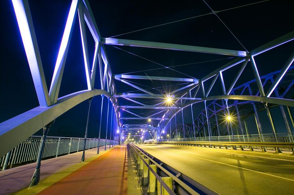 Na fotografii widoczny jest wiadukt na ul. Kościuszki w Gdańsku. Stalowa, ażurowa konstrukcja podświetlona jest na kolor fioletowy. Widoczna jest także dwupasmowa jezdnia i chodnik.