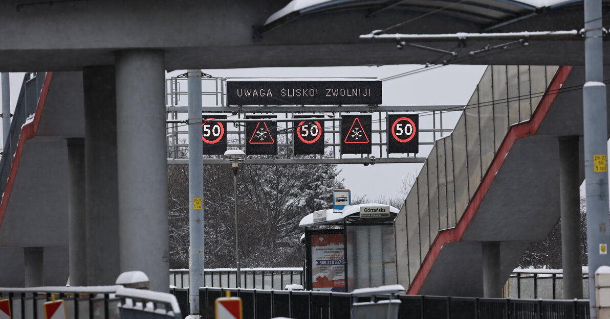 Widoczne tablice ostrzegawcze nad drogą. Znaki drogowe ostrzegające o maksymalnej prędkości 50 km/h oraz napis na tablicy - Uwaga, ślisko.