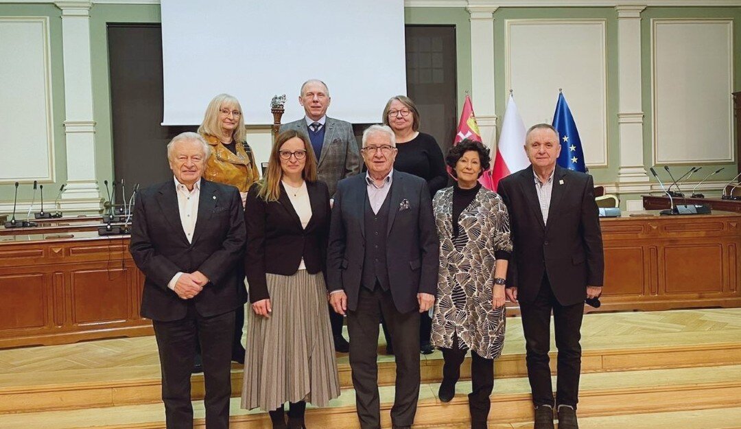 Ośmioro członków nowej Kapituły nagrody stoi w sali obrad Rady Miasta na tle stołów prezydialnych