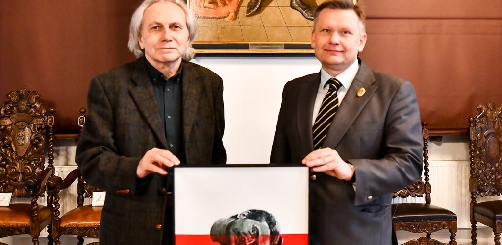 Zdjęcie. Maciej Świeszewski (z lewej) i Waldemar Ossowski (z lewej). Trzymają obraz "Lech". W tle wnętrze Wielkiej Sali Wety w Ratuszu Głównego Miasta. 