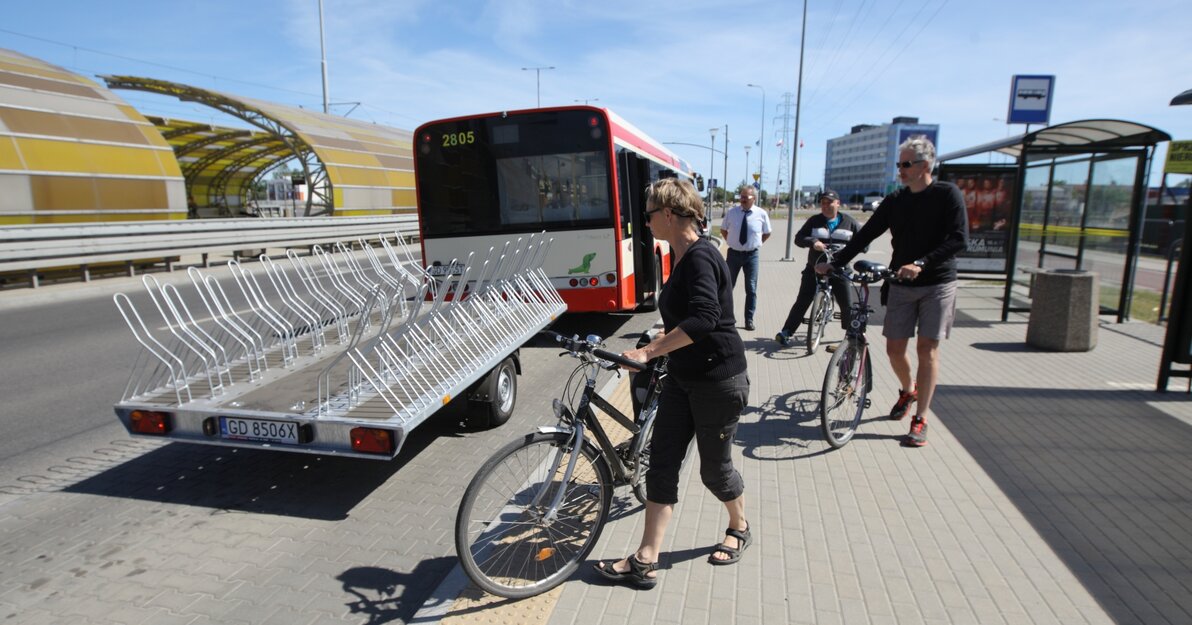 Rowerzyści pakują rowery na przyczepkę zamocowaną do autobusu. 
