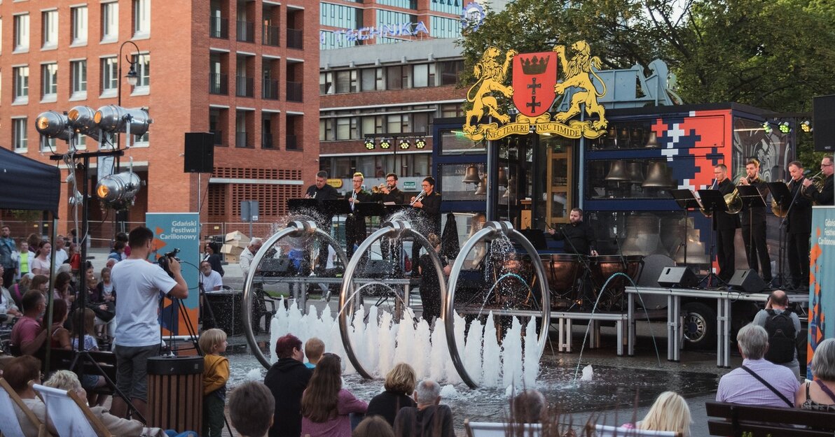 Słuchacze koncertu carillonowego przy skwerze Heweliusza. W tle carillon mobilny "Gdańsk" i zabudowania przy ul. Rajskiej.